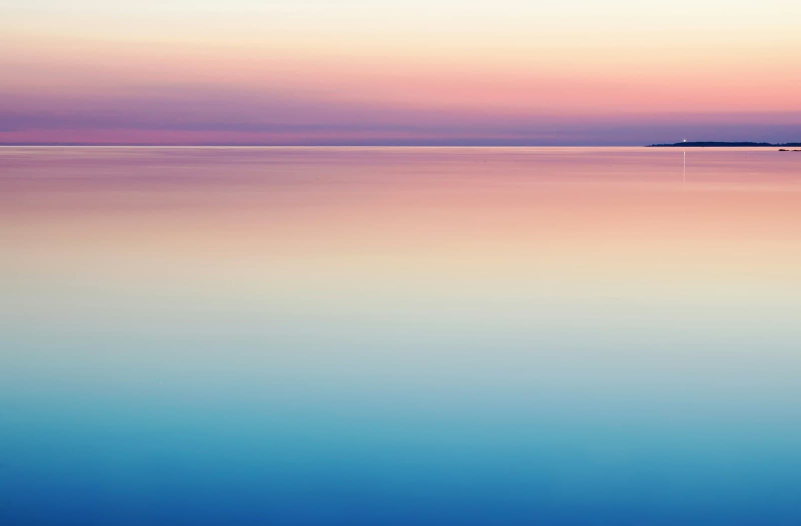 A calm sea fading into a pink and blue horizon at dawn